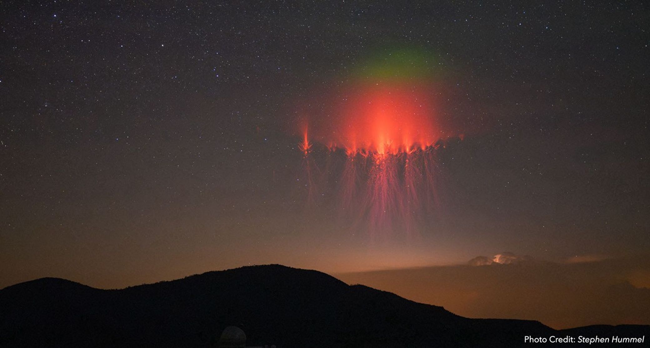 A clearly visible jellyfish-shaped red sprite above distant mountains — Photograph by Stephen Hummel, featured by NASA Science / Spritacular. Original photograph.