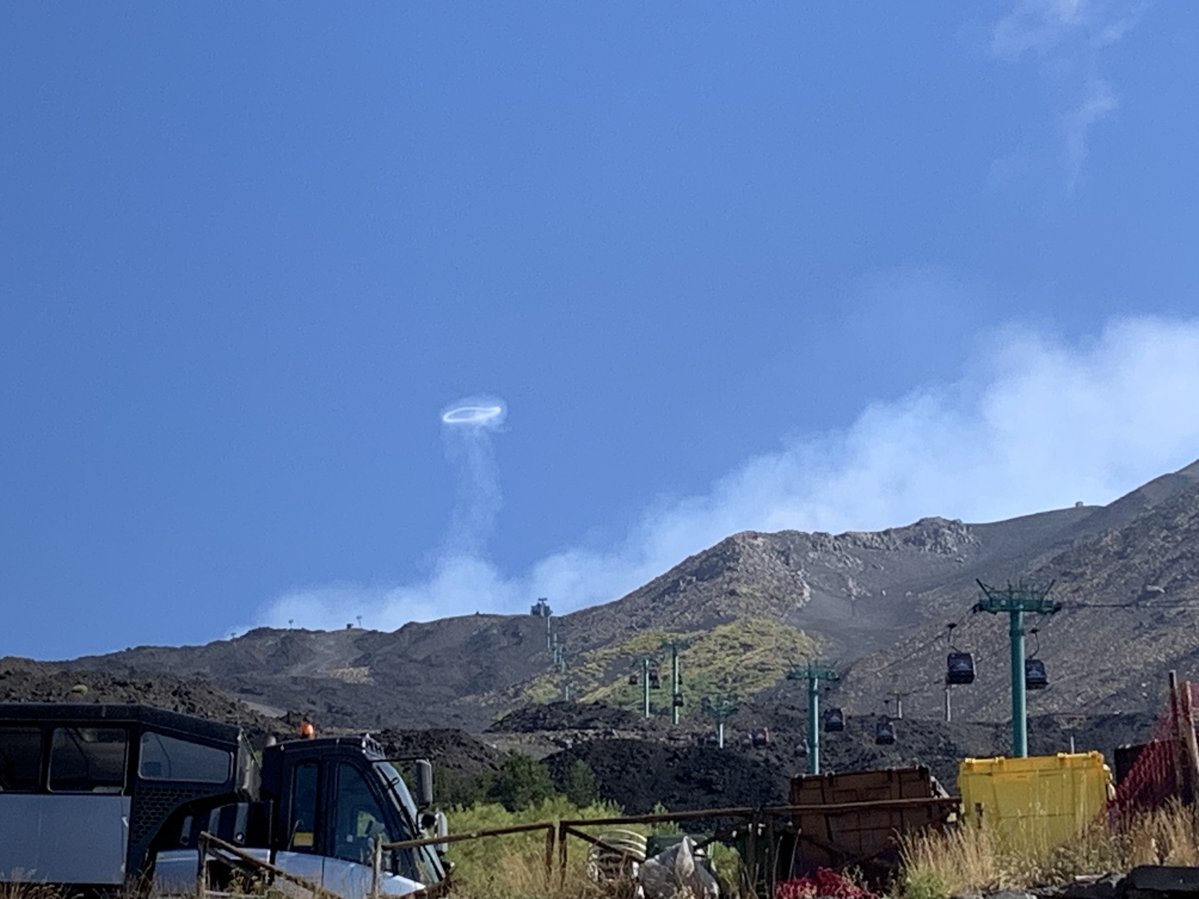 A small gas ring above Mount Etna, with the volcanic landscape and buildings visible below