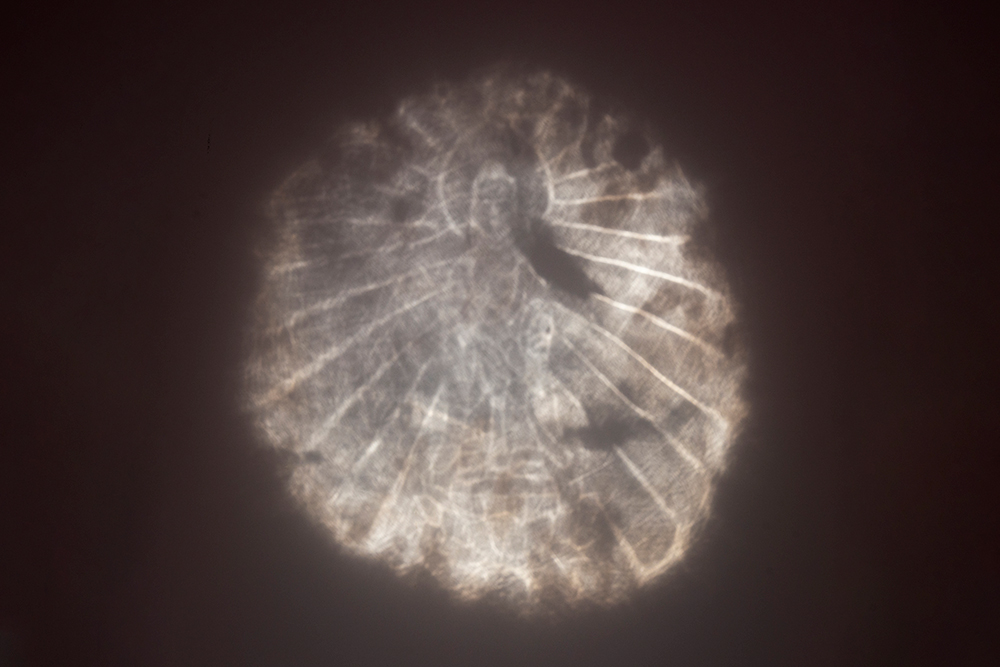 The Buddha image projected by the mirror under directed light — Rob Deslongchamps / Cincinnati Art Museum. Buddhist bronze mirror x1961.2, original photograph.